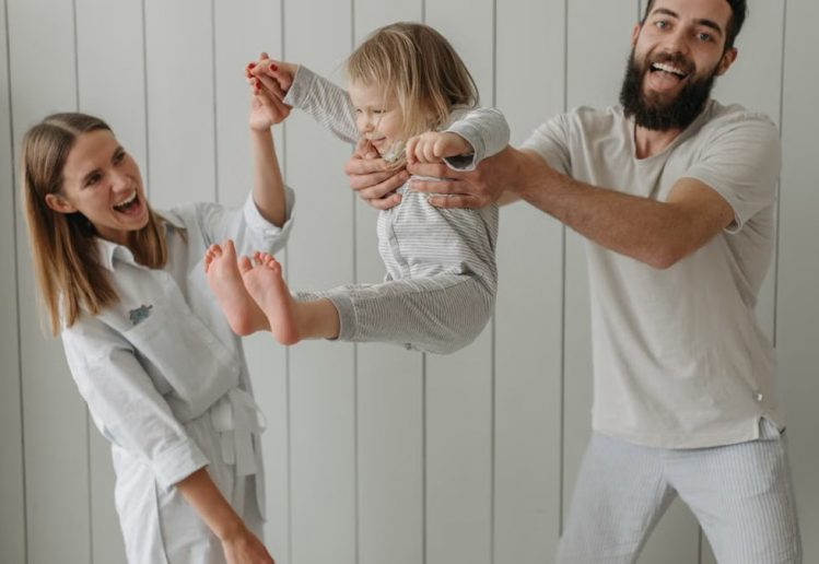 Joyful parents playing with their daughter indoors, all wearing white, capturing a moment of happiness.